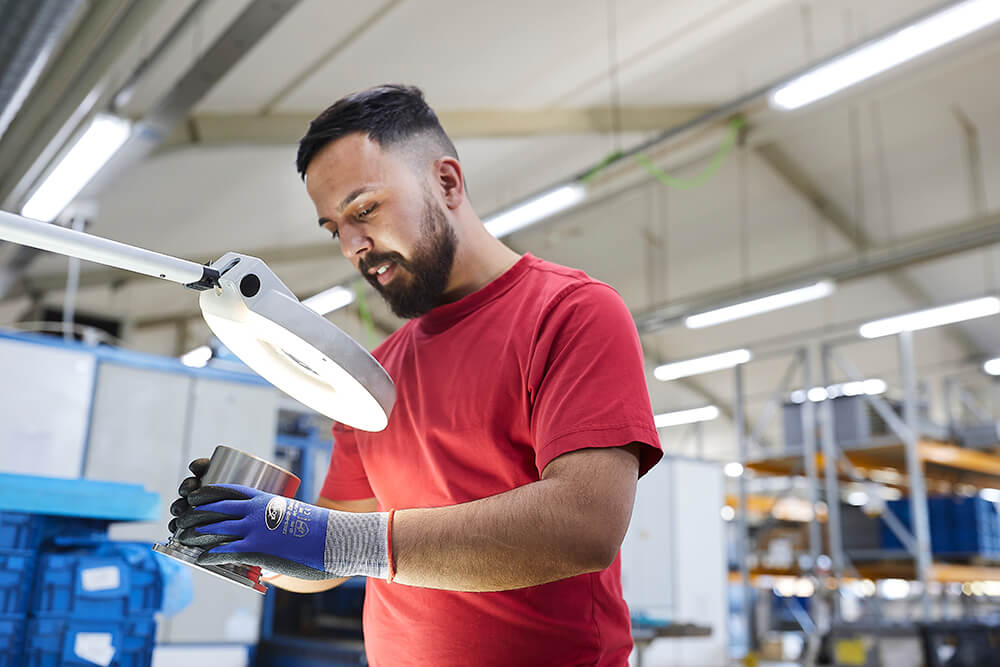 Mitarbeiter prüft Bauteil unter einer Lampe